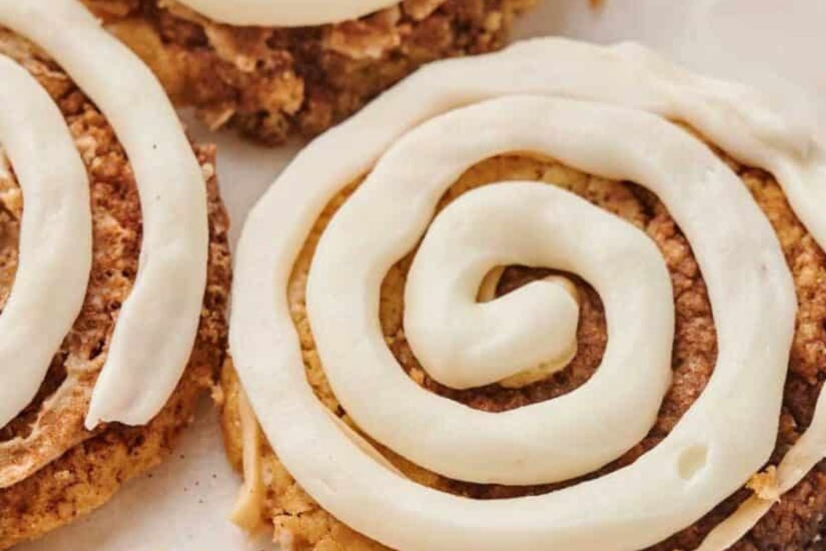 A delectable close-up of Copycat Crumbl Cinnamon Swirl Cookies, adorned with spiral white icing on a parchment paper background.