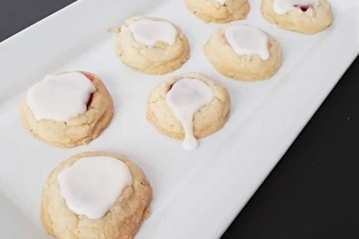 Seven cookies with white icing on a rectangular white plate.