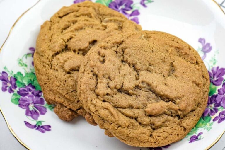 Two brown cookies on a white plate with purple and green floral designs.