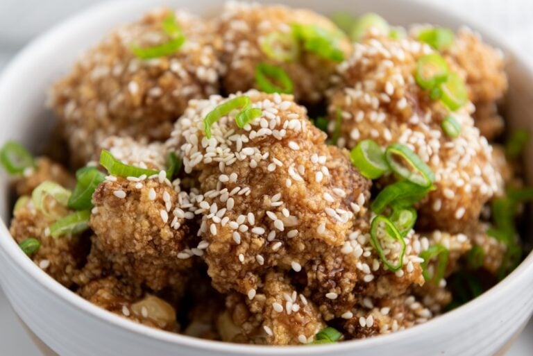 Close-up of a bowl of crispy fried cauliflower topped with sesame seeds and sliced green onions.