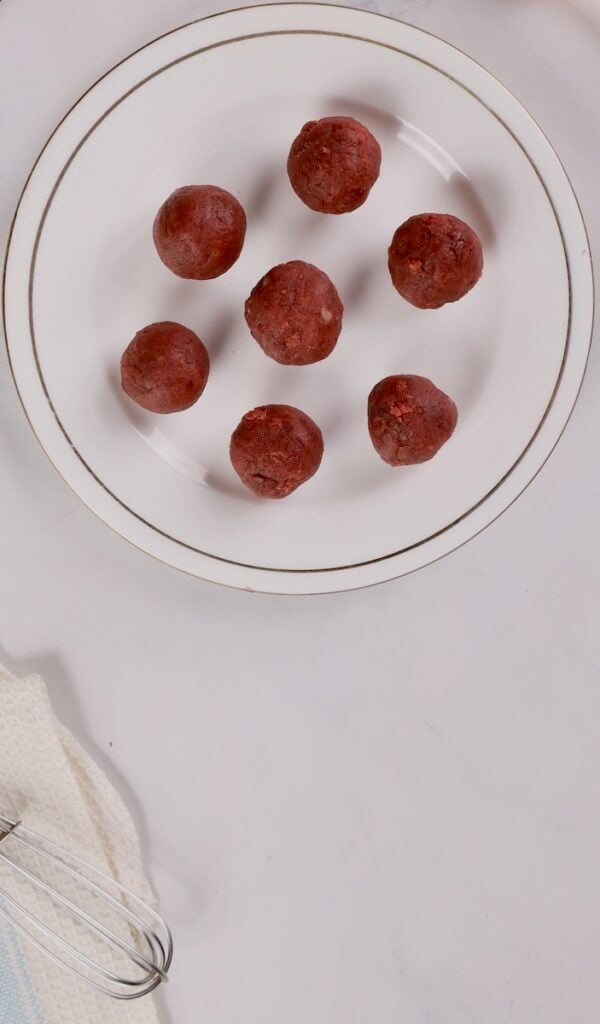 A white plate with seven chocolate truffles arranged in a circle, reminiscent of cake pops in a mug. A whisk and towel are visible in the bottom left corner.