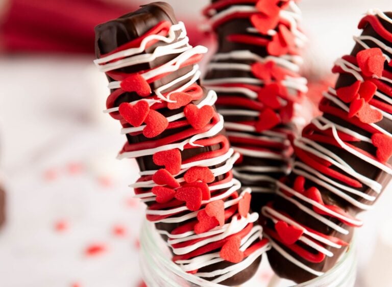 Chocolate-covered pretzel rods decorated with white icing and red heart-shaped sprinkles.