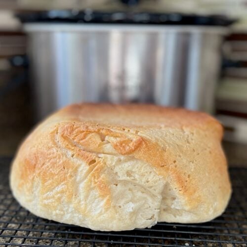 A loaf of crock pot sourdough bread with a golden crust sits on a cooling rack, showcasing its perfect bake.