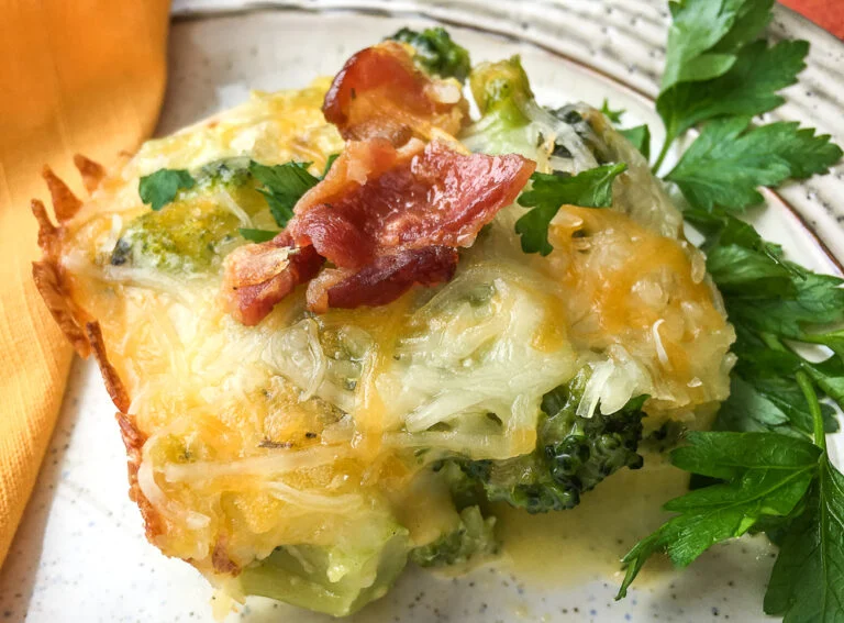 Cheesy broccoli casserole topped with crispy bacon on a plate, garnished with fresh parsley.