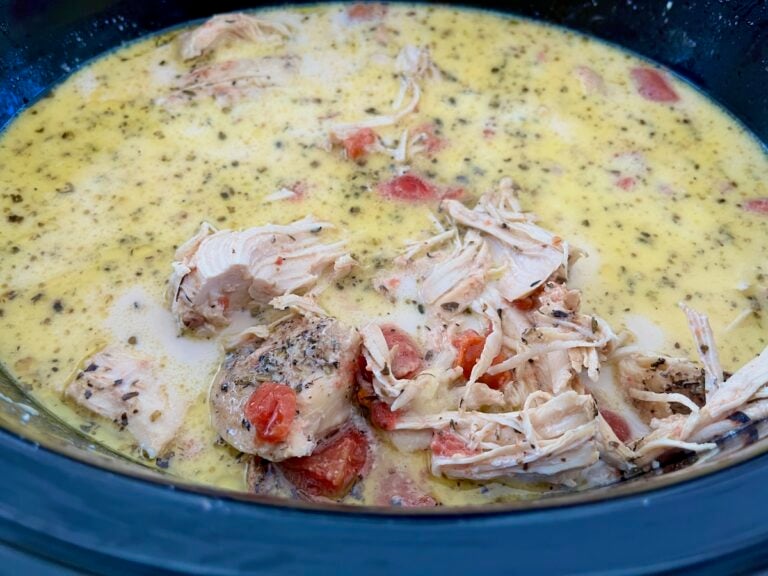 Close-up of a creamy chicken stew with shredded chicken, diced tomatoes, and herbs in a pot.