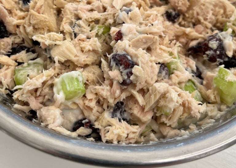 A stainless steel bowl filled with a delightful blend of cranberry tuna salad, featuring succulent shredded chicken, crisp celery, creamy mayonnaise, and bursts of dried cranberries.