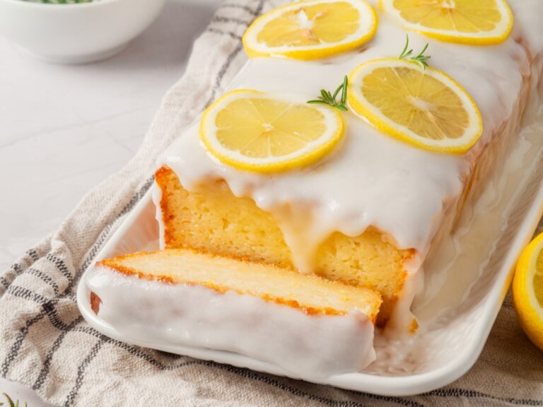 Lemon loaf cake with white icing and lemon slices on top, served on a rectangular plate with a piece cut.