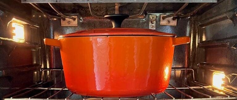 A red Dutch oven with a lid is placed inside an illuminated oven.