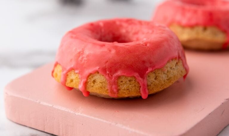 Pink frosted donut on a pink surface, with a second donut partially visible in the background.