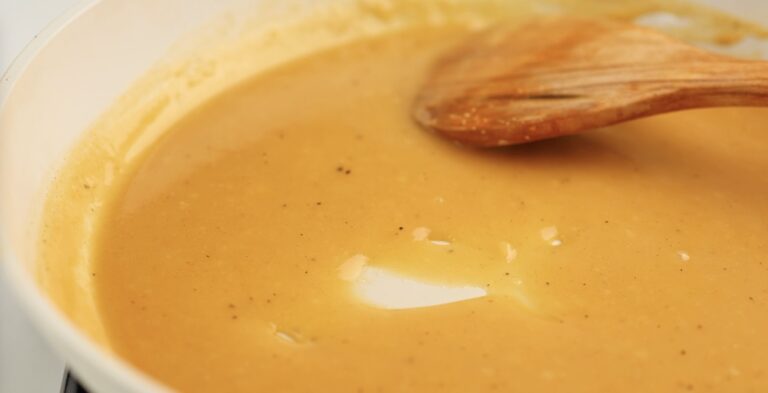 Golden brown gravy in a pan, reminiscent of making a roux, being stirred with a wooden spoon.