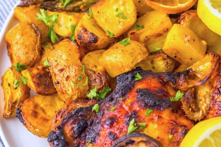 Plate of roasted chicken and potatoes garnished with herbs, alongside lemon slices.