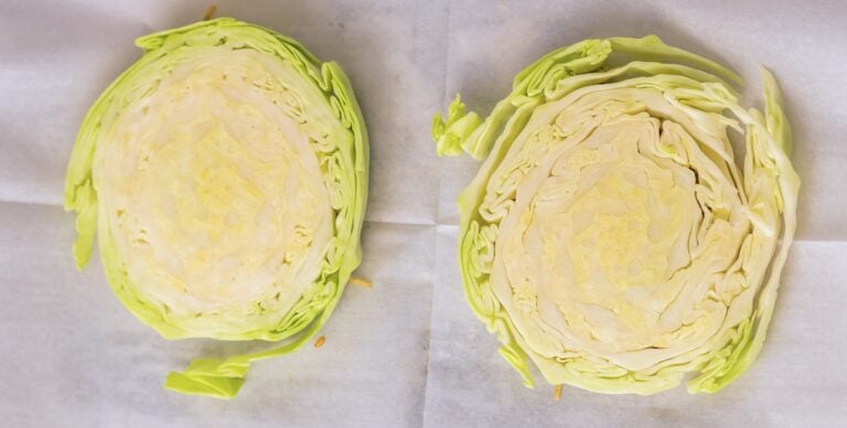 Two halves of a green cabbage placed on a white surface showcase the intricate concentric leaf structure, highlighting one of the fascinating kinds of cabbage.