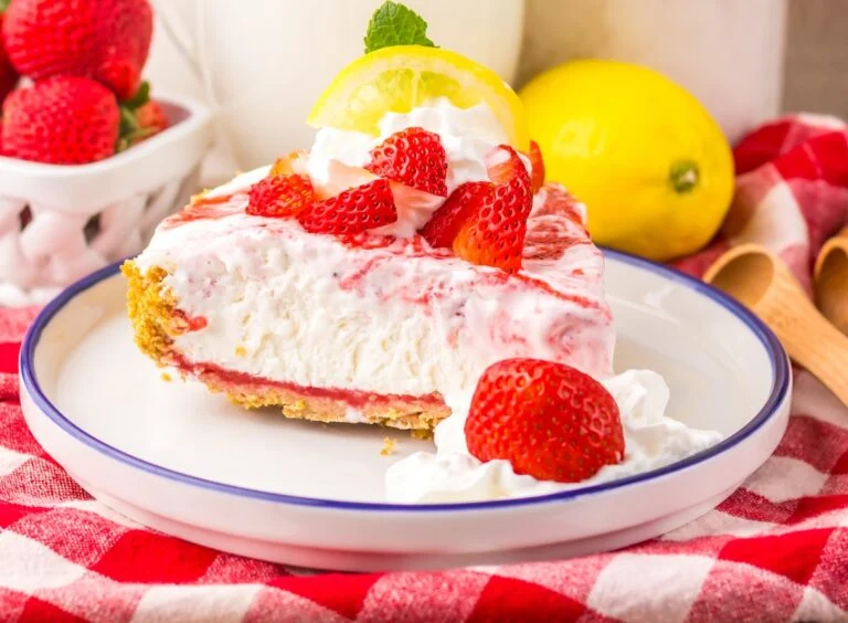 A slice of strawberry lemon cream pie topped with whipped cream, fresh strawberries, and a lemon slice, served on a white plate with a blue rim.
