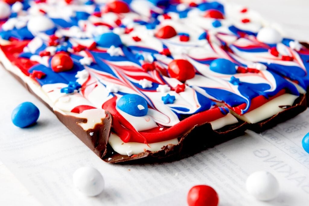 A chocolate bark topped with swirled red, white, and blue candy melts and decorated with star-shaped sprinkles and candy-coated chocolates.