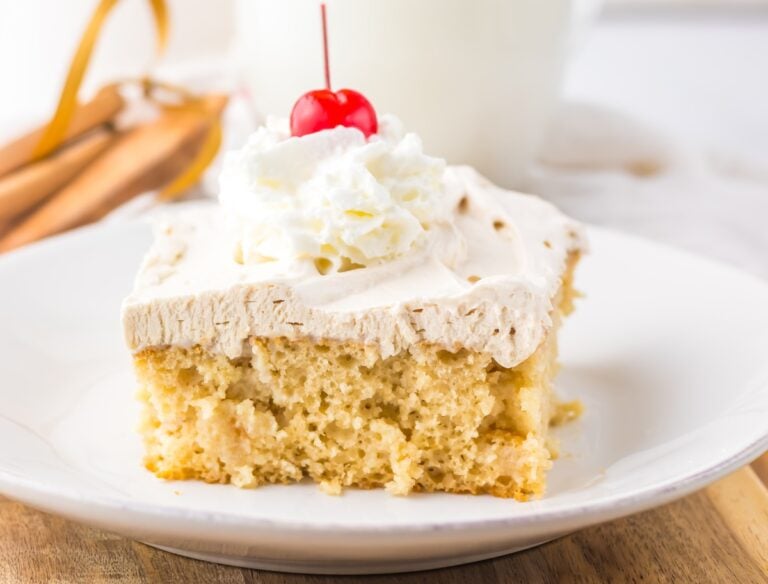 A slice of Tres Leches cake topped with whipped cream and a cherry on a white plate.