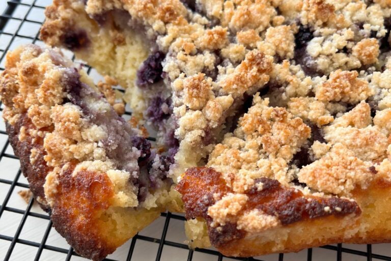 Close-up of a blueberry crumb cake on a cooling rack, with visible layers of moist cake, blueberry filling, and crumb topping.