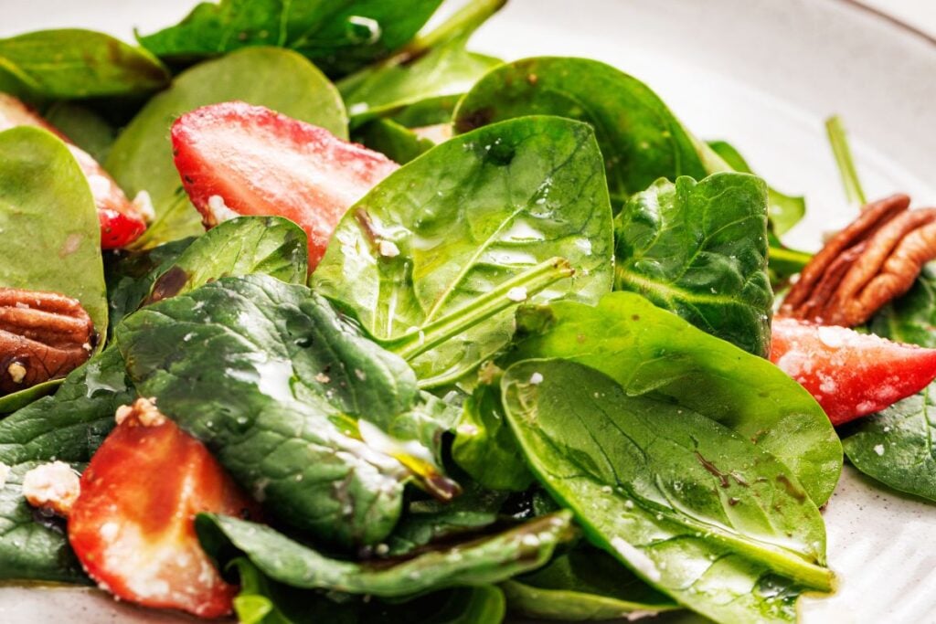 A close-up of a spinach salad with strawberries, pecans, and a sprinkle of feta cheese on a white plate.