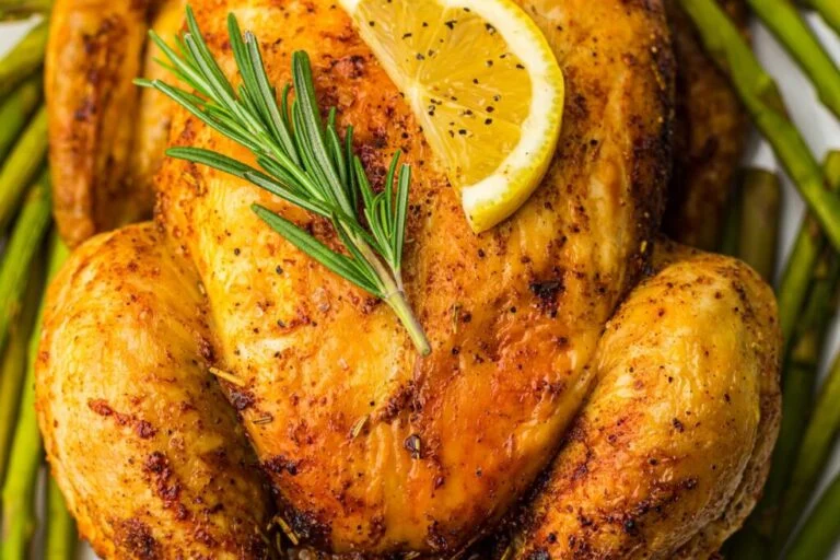 Roasted chicken garnished with a lemon slice and rosemary sprig, surrounded by asparagus spears.