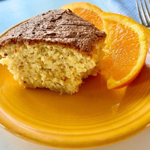 A slice of cake on a yellow plate, accompanied by two slices of orange, with a fork to the side.