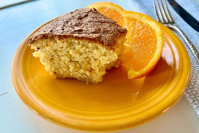 A slice of cake on a yellow plate, accompanied by two slices of orange, with a fork to the side.