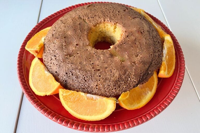 Round cake on a red plate, surrounded by orange slices.