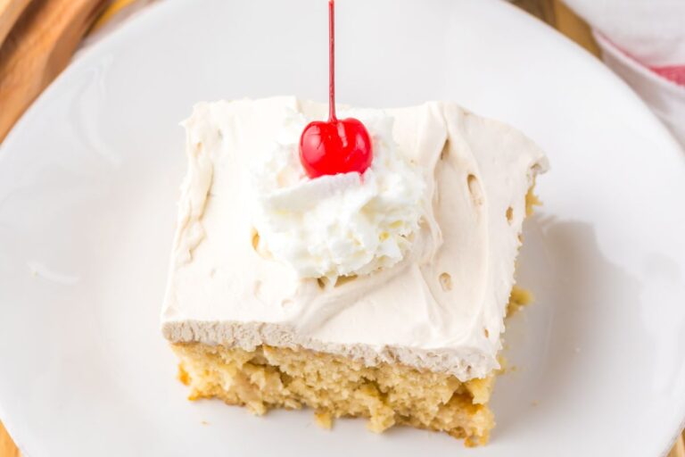 A slice of cake topped with whipped cream and a red cherry on a white plate.