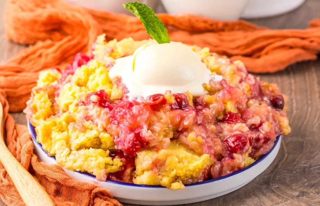 A serving of fruit cobbler topped with a scoop of vanilla ice cream and a mint leaf, presented in a shallow dish on a wooden table.