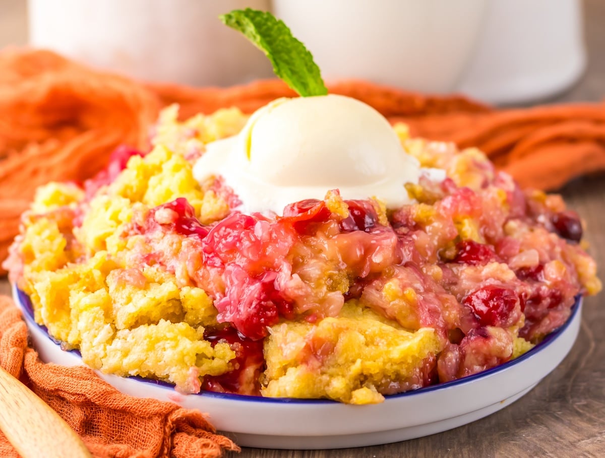 A close-up of a baked peach cobbler topped with a scoop of vanilla ice cream and a mint leaf in a white dish.