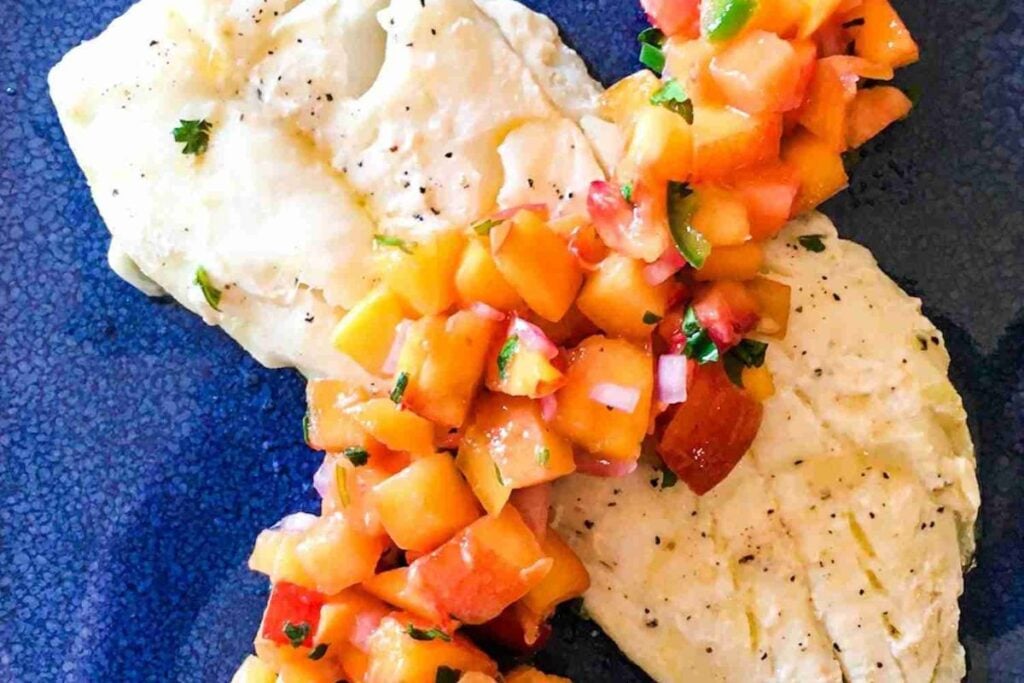 Two grilled white fish fillets topped with a peach and tomato salsa, served on a dark blue plate.