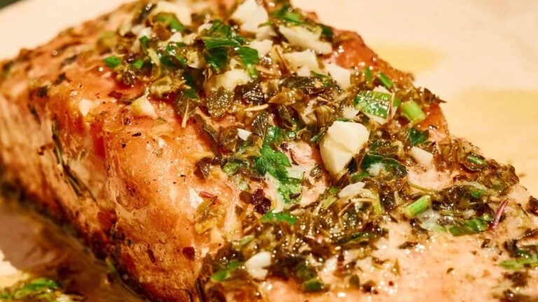 A close-up of a cooked salmon fillet topped with a mixture of chopped herbs, garlic, and seasonings.