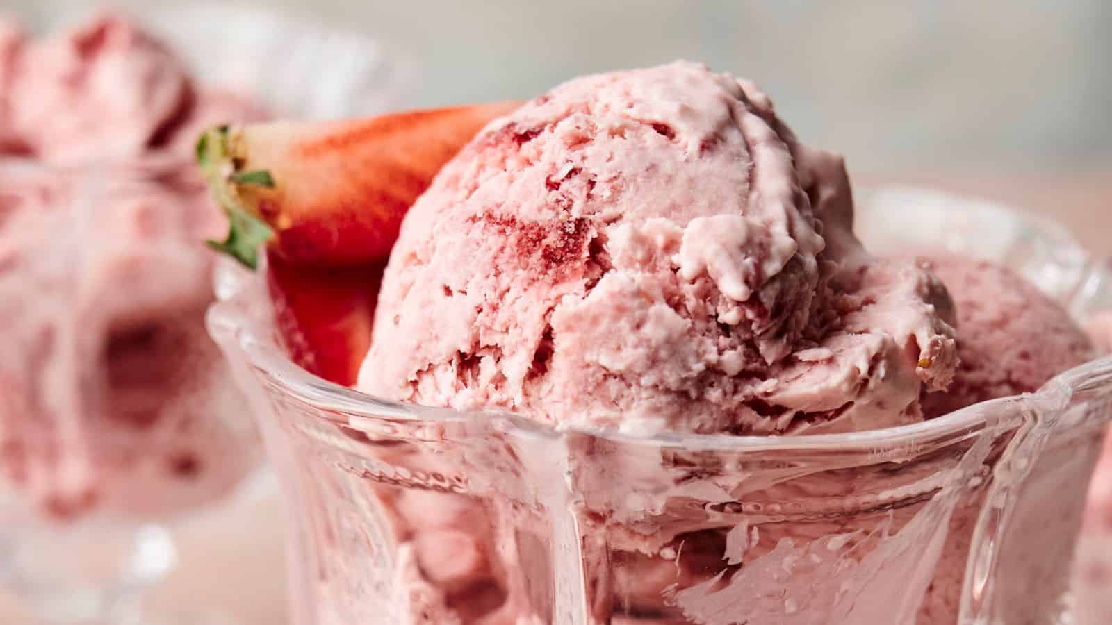 Close-up of scoops of strawberry ice cream in a glass dish, garnished with a fresh strawberry.