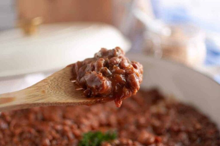 A wooden spoon holding a serving of chili with beans over a pot of more chili in the background.