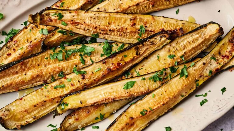 Roasted zucchini halves garnished with chopped parsley arranged on a white plate.