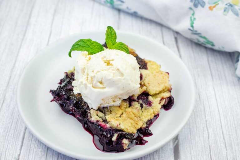 A serving of berry cobbler topped with a scoop of vanilla ice cream and a mint sprig on a white plate.