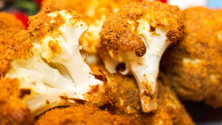 Close-up of several pieces of cauliflower coated in a golden, crispy breading, suggesting they are baked or fried.