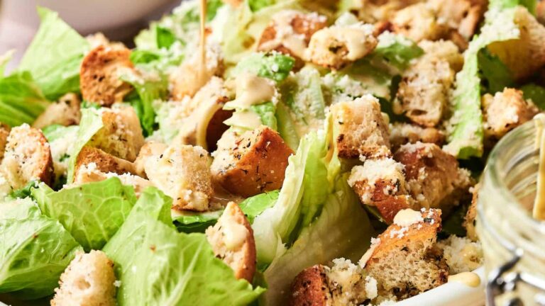 A close-up of Caesar salad with romaine lettuce, croutons, grated cheese, and dressing.