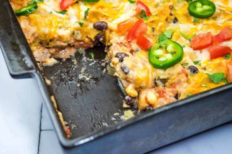 A partially eaten baked casserole with melted cheese, black beans, corn, tomatoes, and jalapeño slices in a rectangular pan.