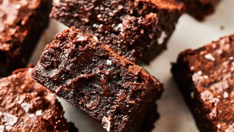 Close-up of several rich, fudgy chocolate brownies topped with flakes of sea salt.