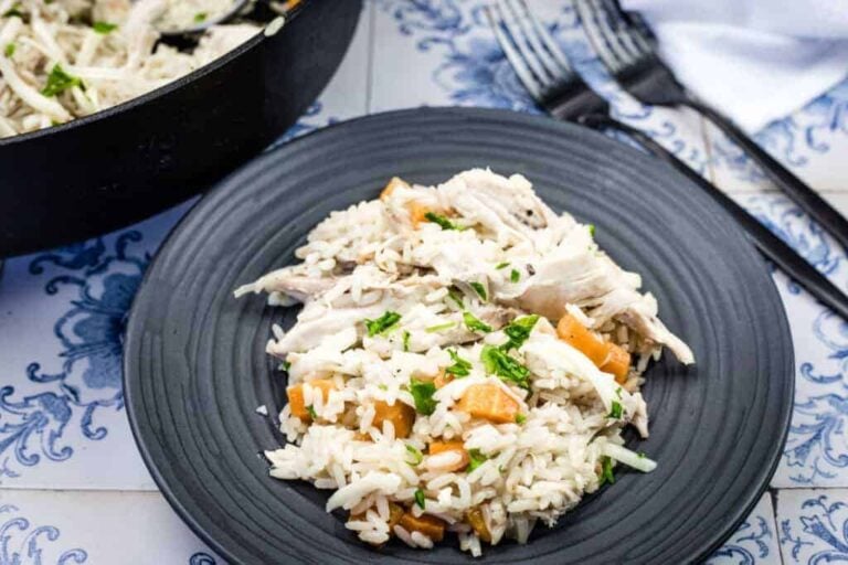 A black plate with a serving of rice mixed with shredded chicken, diced carrots, and chopped herbs; two forks are beside the plate.