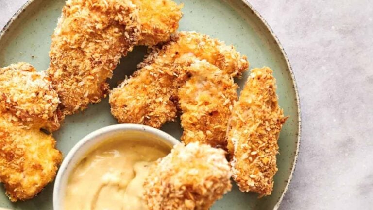 A plate of breaded chicken tenders is arranged around a small bowl of dipping sauce.
