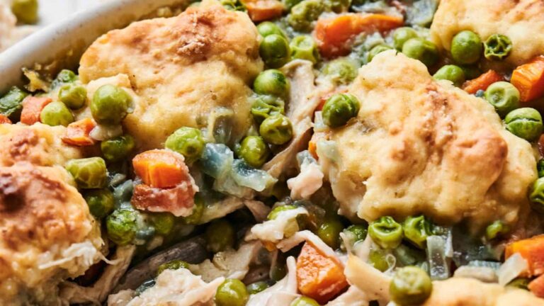 Close-up of a baked dish with biscuits on top, featuring peas, carrots, shredded chicken, and a creamy sauce.