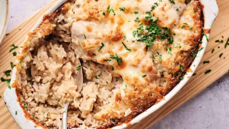 A baked casserole dish filled with creamy rice and melted cheese, garnished with chopped parsley, with a spoon scooping out a portion.