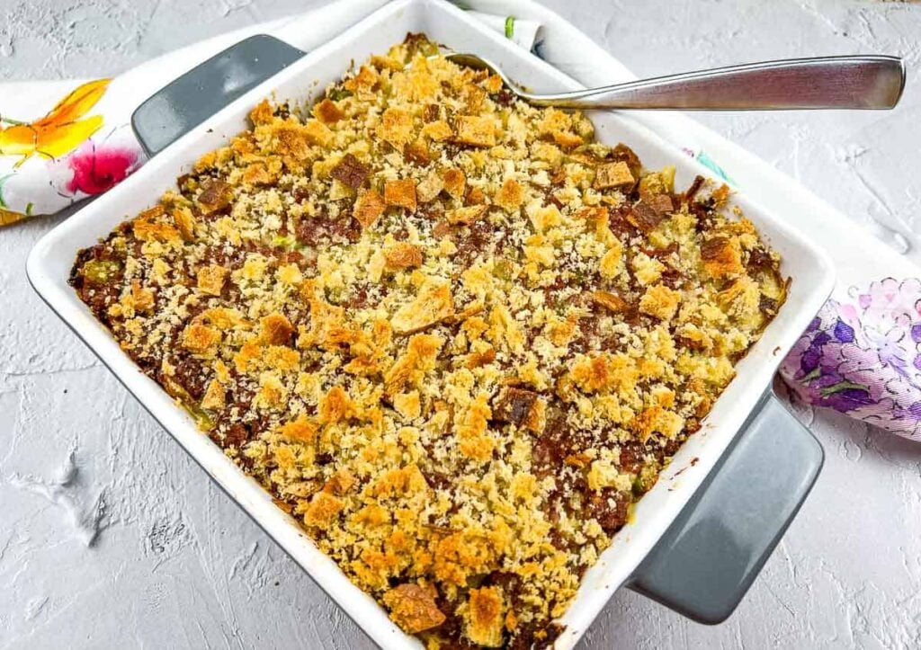 A baked casserole topped with a golden breadcrumb crust sits in a white baking dish with a serving spoon on the side.