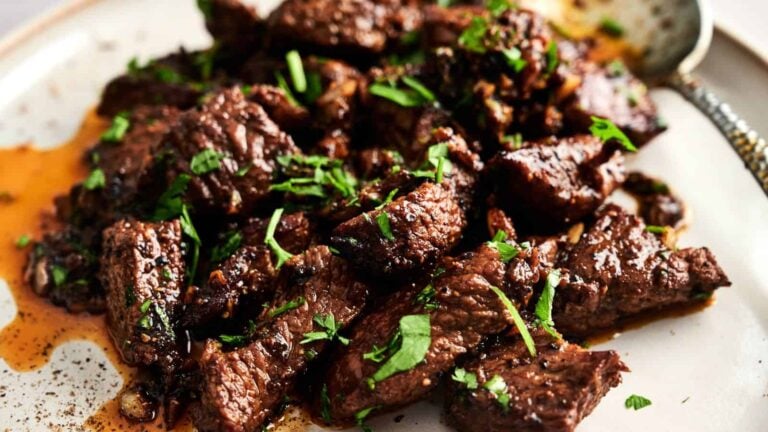 Chunks of cooked beef garnished with chopped fresh herbs are served on a plate with some sauce.