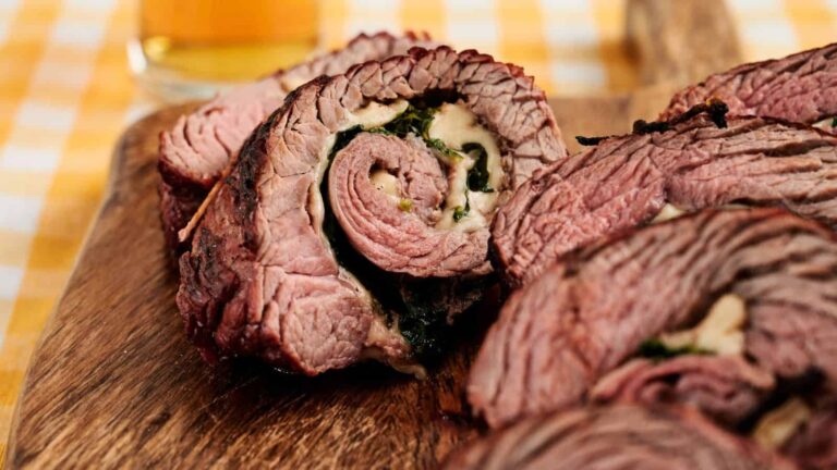 Sliced stuffed flank steak filled with cheese and spinach, served on a wooden cutting board.