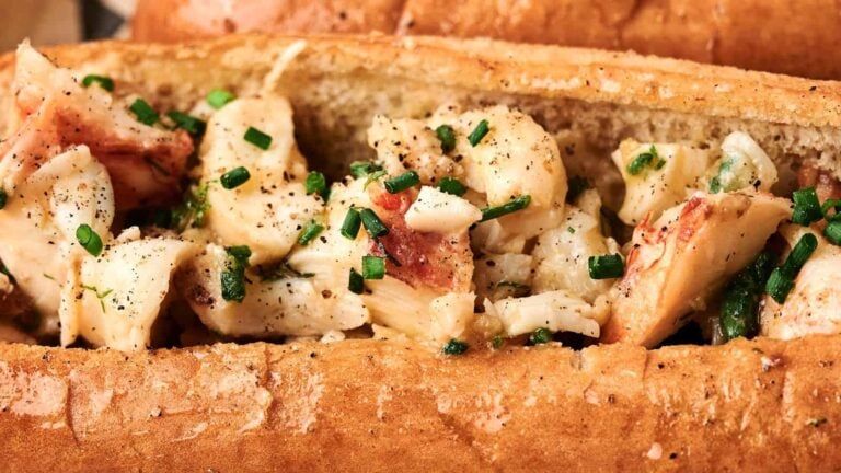 Close-up of a lobster roll with chunks of lobster meat, chopped chives, black pepper, and a split-top toasted bun.