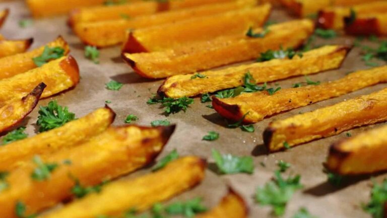 Baked butternut squash fries arranged on a parchment-lined tray, garnished with chopped fresh parsley.