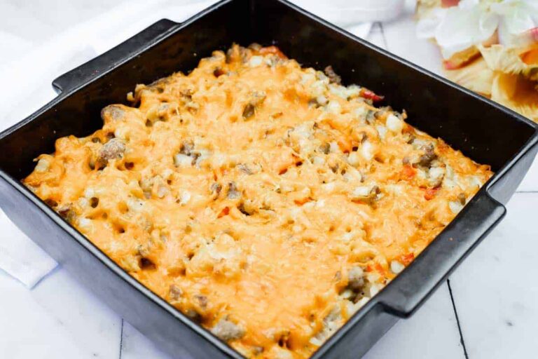 A square baking dish filled with a baked casserole topped with melted cheese and visible chunks of sausage and vegetables.