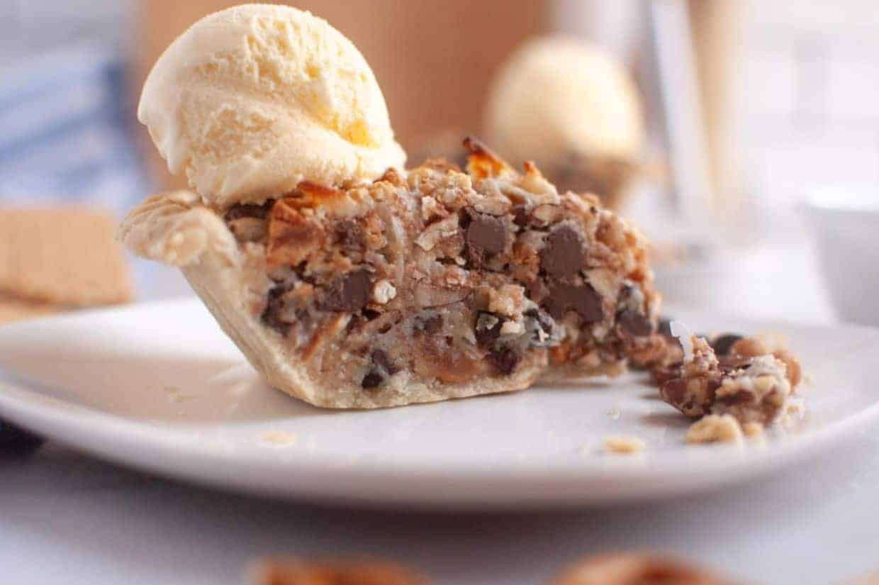 A slice of Texas Trash Pie topped with a scoop of vanilla ice cream, sits on a white plate.