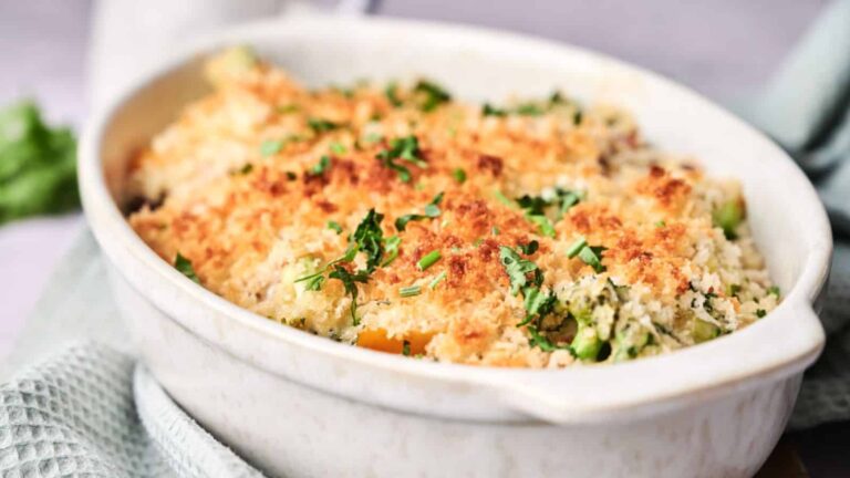 A baked vegetable casserole topped with golden breadcrumbs and garnished with chopped herbs, served in a white oval dish.